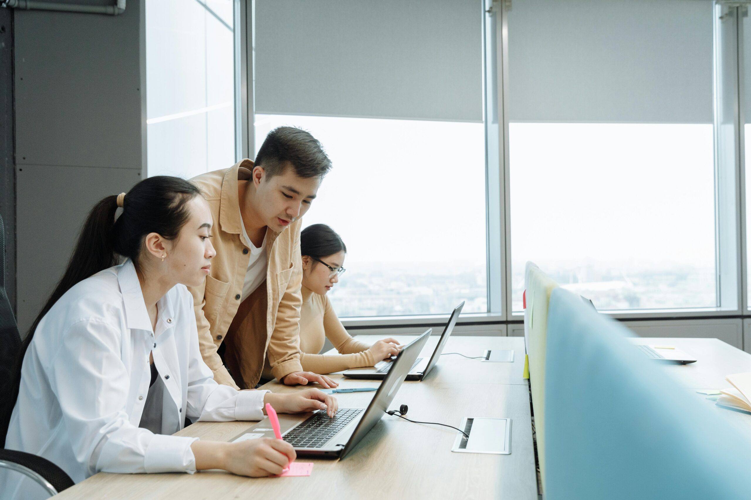 Three colleagues working together on laptops in a bright, modern office space.